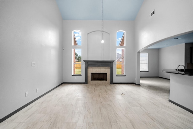 unfurnished living room featuring a tiled fireplace, sink, and high vaulted ceiling