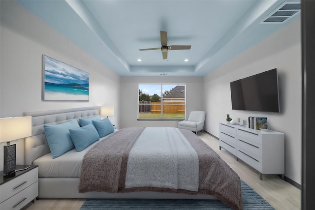 bedroom with light hardwood / wood-style floors, a raised ceiling, and ceiling fan