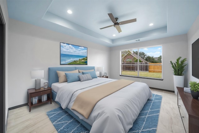 bedroom with ceiling fan, a raised ceiling, and light wood-type flooring