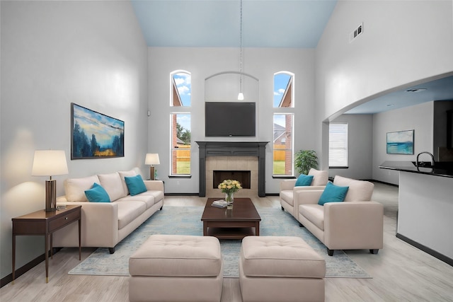 living room featuring light hardwood / wood-style floors, sink, high vaulted ceiling, and a tiled fireplace