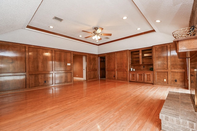 unfurnished living room featuring light hardwood / wood-style flooring, a raised ceiling, a textured ceiling, and wood walls