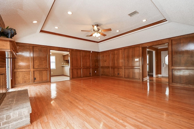 unfurnished living room with a raised ceiling, ornamental molding, a textured ceiling, and light hardwood / wood-style flooring