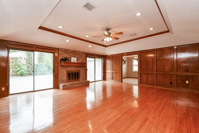 unfurnished living room featuring light hardwood / wood-style flooring, a wealth of natural light, a fireplace, and a tray ceiling