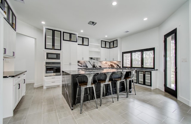 kitchen featuring black microwave, oven, a spacious island, a breakfast bar, and white cabinets