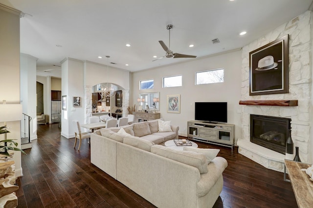 living room with a stone fireplace, crown molding, dark hardwood / wood-style flooring, and ceiling fan with notable chandelier