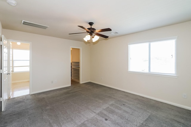 spare room featuring a wealth of natural light, ceiling fan, and dark carpet