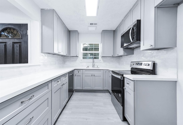 kitchen with gray cabinetry, sink, stainless steel appliances, light hardwood / wood-style flooring, and backsplash