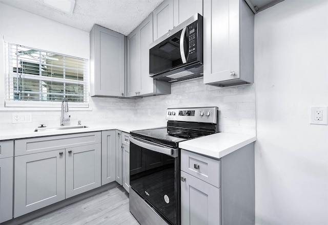 kitchen with appliances with stainless steel finishes, light wood-type flooring, tasteful backsplash, gray cabinetry, and sink