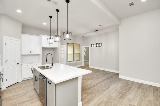 kitchen with decorative light fixtures, sink, white cabinetry, and an island with sink