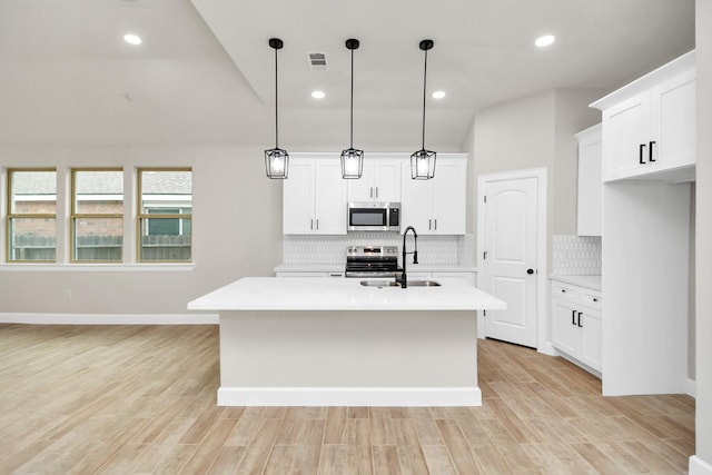 kitchen featuring appliances with stainless steel finishes, sink, pendant lighting, a center island with sink, and light hardwood / wood-style flooring