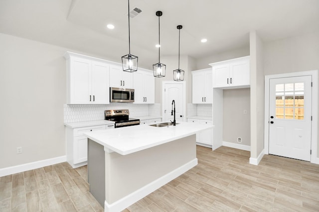 kitchen with sink, hanging light fixtures, stainless steel appliances, a center island with sink, and light wood-type flooring