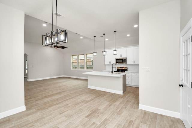 kitchen featuring white cabinets, decorative light fixtures, an island with sink, and appliances with stainless steel finishes