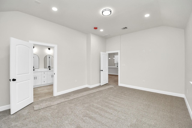 unfurnished bedroom featuring vaulted ceiling, light colored carpet, and ensuite bath