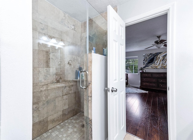 bathroom with ceiling fan, an enclosed shower, wood-type flooring, and a textured ceiling