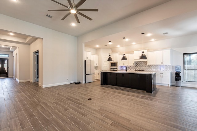 kitchen with white cabinets, white fridge, light wood-type flooring, and an island with sink