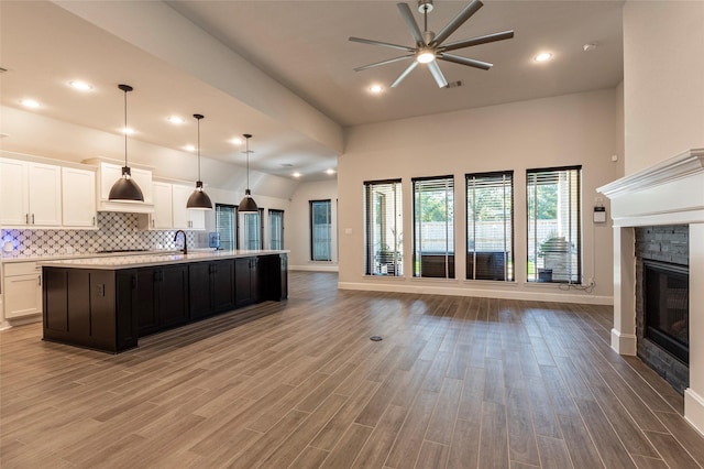 kitchen featuring a fireplace, a kitchen island with sink, hanging light fixtures, and light hardwood / wood-style flooring