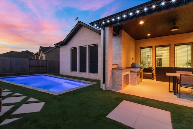 pool at dusk with a lawn, grilling area, a patio area, and exterior kitchen