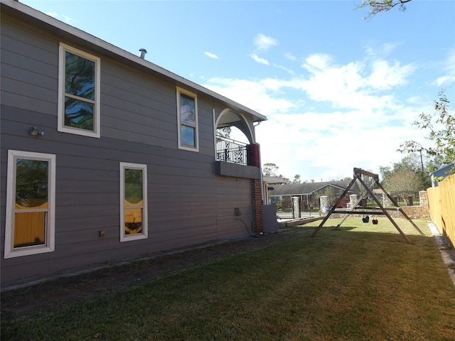 view of side of property with a playground, a balcony, and a lawn