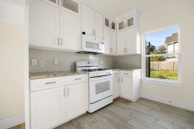 kitchen with tasteful backsplash, light stone counters, white appliances, light hardwood / wood-style flooring, and white cabinets