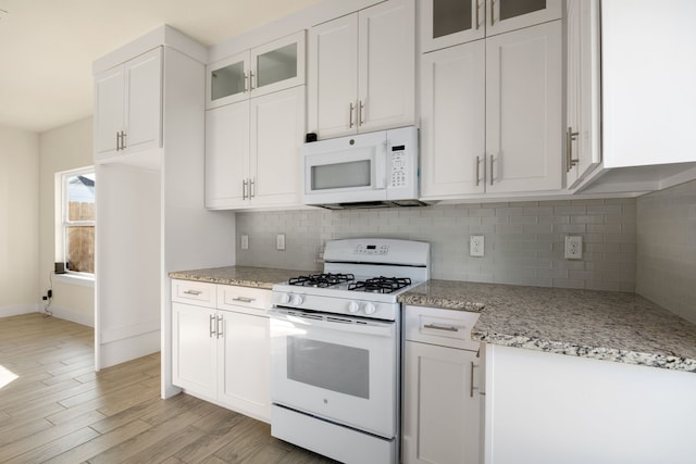 kitchen with backsplash, light stone counters, white appliances, light hardwood / wood-style flooring, and white cabinetry