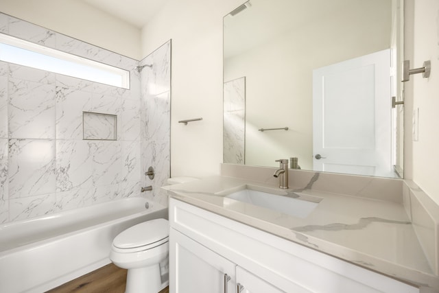 full bathroom featuring hardwood / wood-style flooring, tiled shower / bath combo, toilet, and vanity