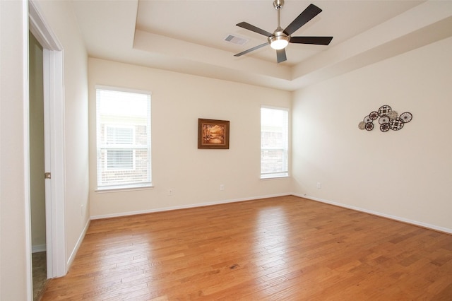 unfurnished room featuring plenty of natural light, ceiling fan, light wood-type flooring, and a tray ceiling