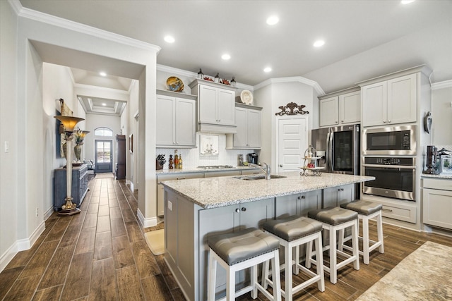 kitchen with a center island with sink, sink, appliances with stainless steel finishes, light stone counters, and a breakfast bar area