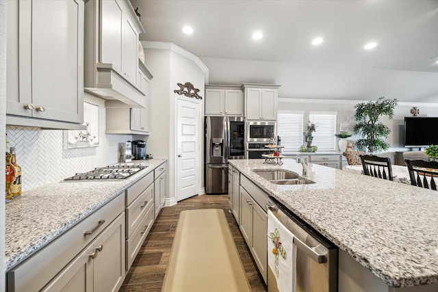 kitchen with light stone counters, stainless steel appliances, a kitchen island with sink, dark wood-type flooring, and sink