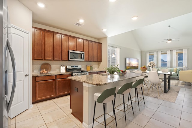 kitchen featuring a kitchen bar, appliances with stainless steel finishes, light stone countertops, lofted ceiling, and an island with sink