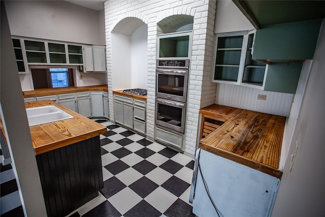 kitchen featuring wooden counters, sink, white cabinetry, appliances with stainless steel finishes, and brick wall