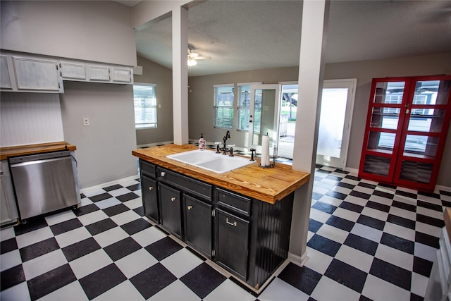 kitchen with lofted ceiling, wooden counters, stainless steel dishwasher, a wealth of natural light, and sink