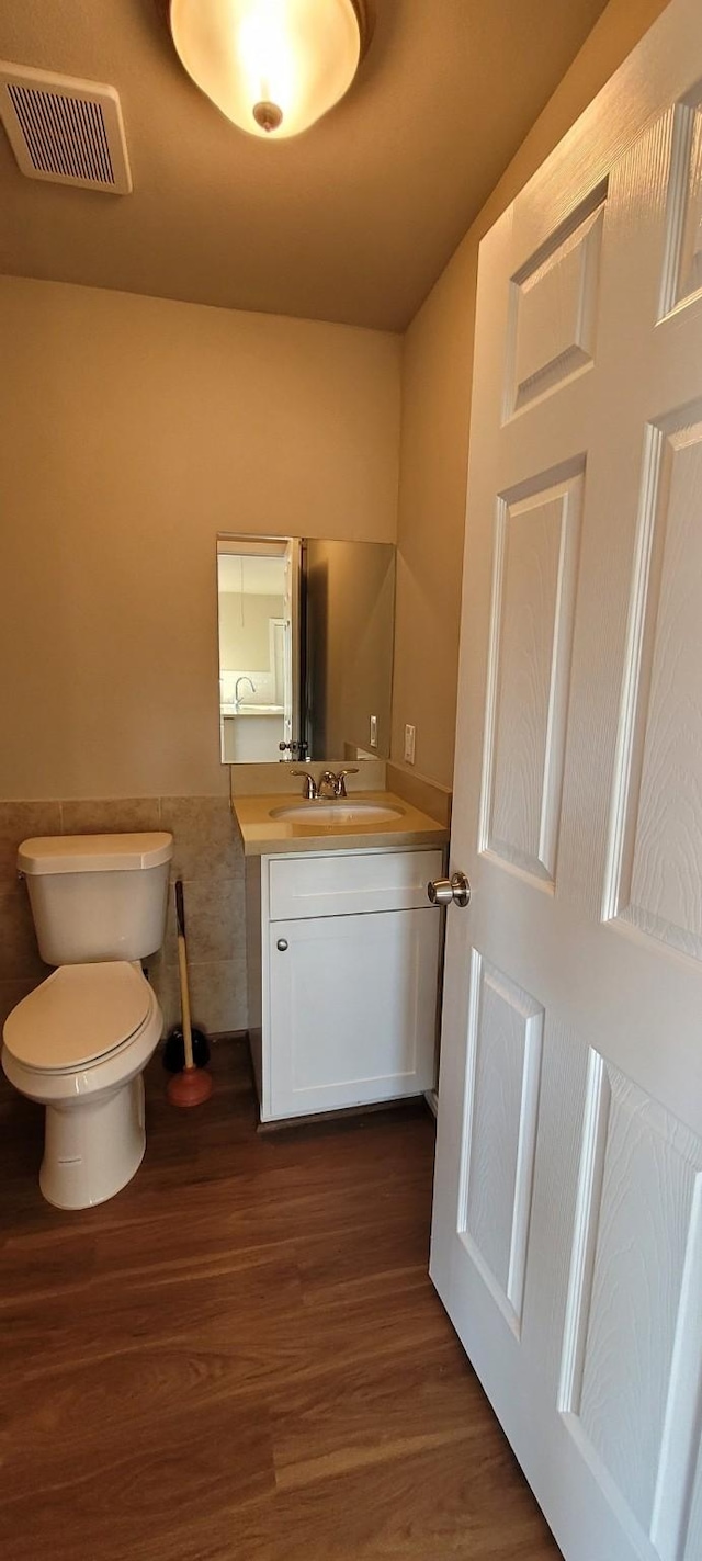 bathroom with wood-type flooring, vanity, toilet, and tile walls