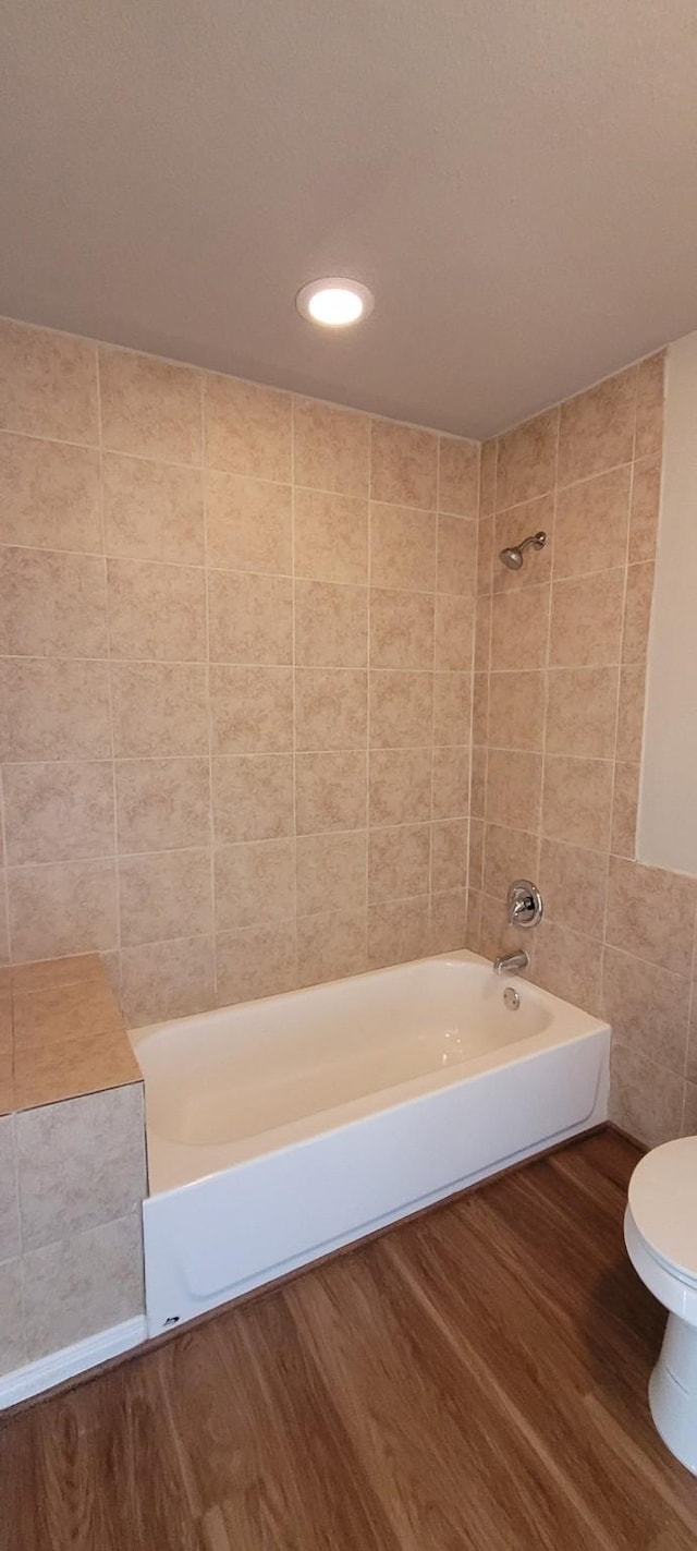 bathroom featuring toilet, wood-type flooring, tile walls, and tiled shower / bath