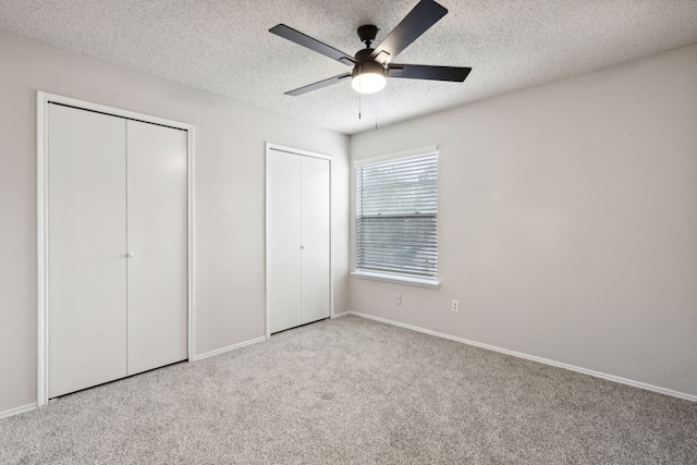 unfurnished bedroom with a textured ceiling, ceiling fan, light colored carpet, and two closets