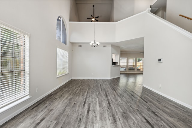 unfurnished living room with a high ceiling, ceiling fan with notable chandelier, and dark hardwood / wood-style floors