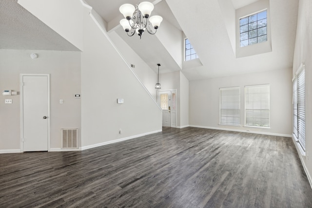 unfurnished living room featuring a wealth of natural light, dark hardwood / wood-style flooring, high vaulted ceiling, and a chandelier