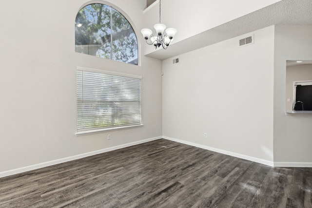 spare room with a wealth of natural light, dark wood-type flooring, a chandelier, and a high ceiling