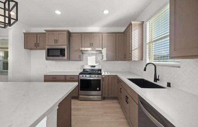 kitchen featuring pendant lighting, sink, light hardwood / wood-style flooring, decorative backsplash, and stainless steel appliances