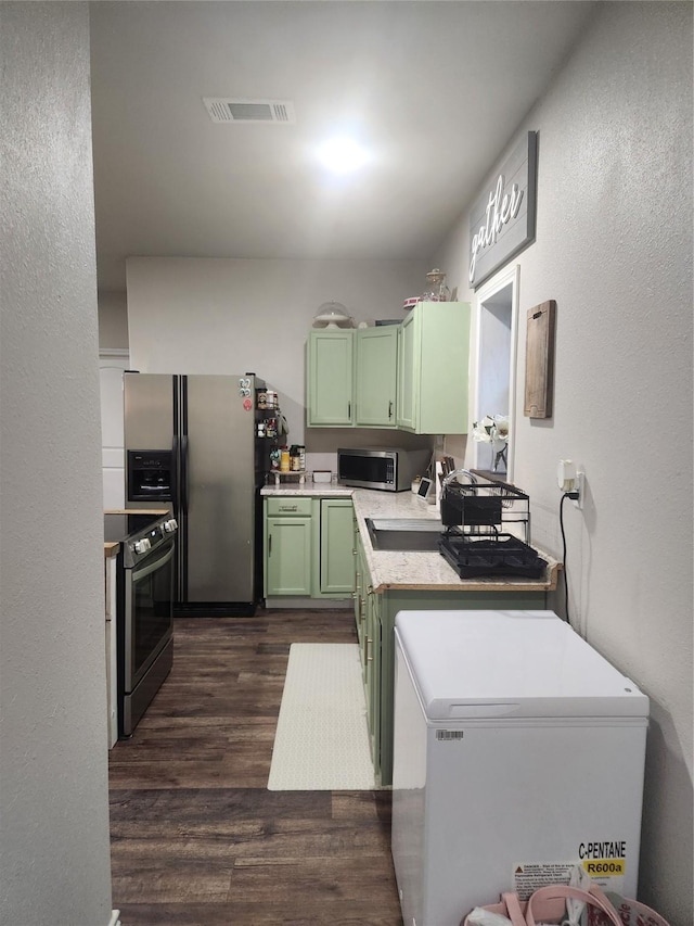 1000 Fm 224th Rd, Coldspring, TX 77331 - kitchen with green cabinetry, appliances with stainless steel finishes, dark wood-style flooring, light countertops, and a textured wall