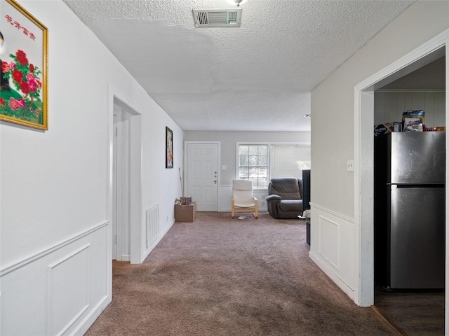 hall featuring carpet flooring and a textured ceiling