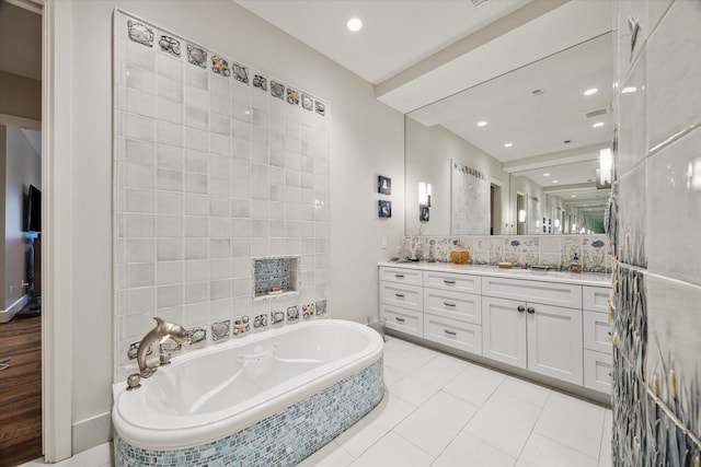 bathroom featuring tile patterned flooring, vanity, tiled bath, and backsplash