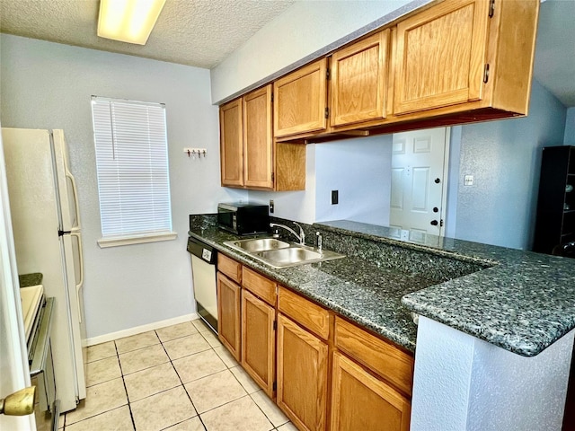 kitchen with white appliances, dark stone counters, sink, light tile patterned floors, and a textured ceiling