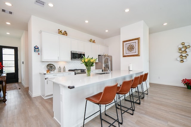 kitchen featuring light wood-type flooring, a breakfast bar, stainless steel appliances, sink, and white cabinetry