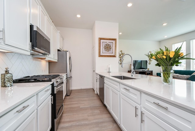 kitchen featuring white cabinetry, sink, stainless steel appliances, light hardwood / wood-style flooring, and decorative backsplash