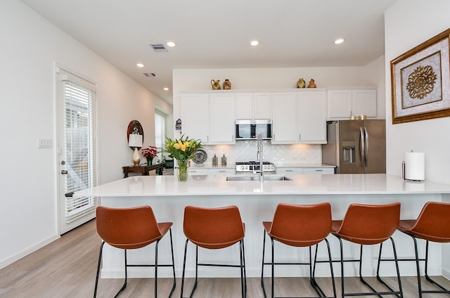 kitchen featuring white cabinets, decorative backsplash, light wood-type flooring, appliances with stainless steel finishes, and a kitchen bar