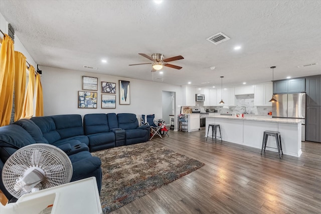 living room with a textured ceiling, ceiling fan, sink, and dark wood-type flooring