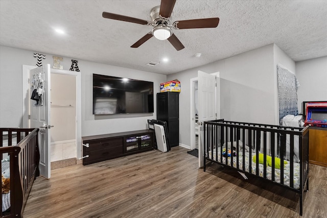 bedroom featuring ceiling fan, a nursery area, a textured ceiling, and hardwood / wood-style flooring