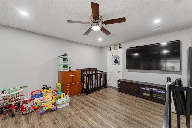 bedroom featuring a textured ceiling, ceiling fan, a crib, and hardwood / wood-style flooring