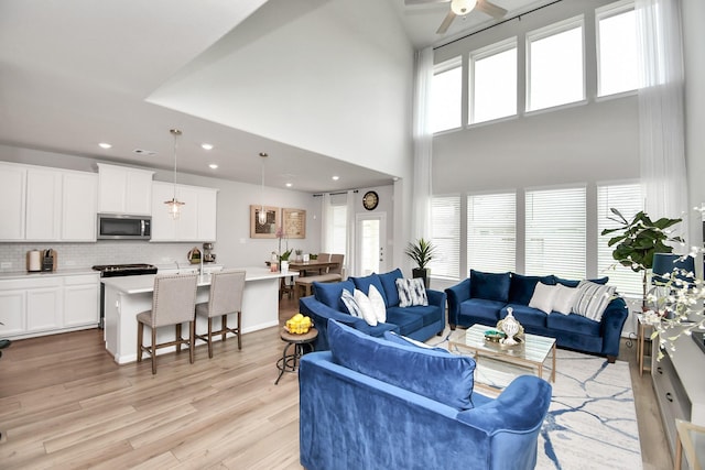 living room with a high ceiling, light wood-type flooring, and ceiling fan