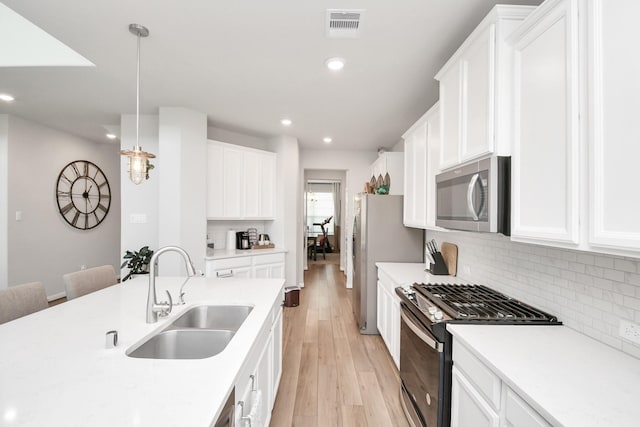 kitchen with sink, stainless steel appliances, decorative light fixtures, white cabinets, and light wood-type flooring